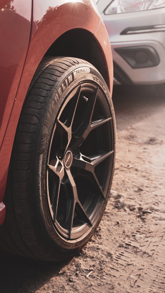 Detailed view of a red car's wheel on a dirt road, showcasing tire tread and custom rim design.